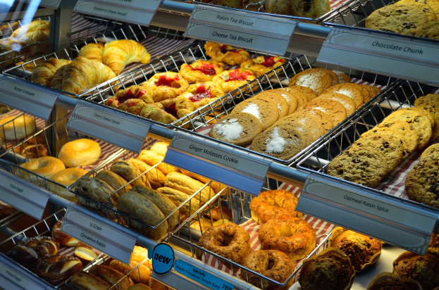 Ein Bäckereischaufenster voller verschiedener Keks- und Kuchensorten, Keks- und Kuchenplatten sowie Schilder mit Aufschriften, die die Art der Backwaren angeben.