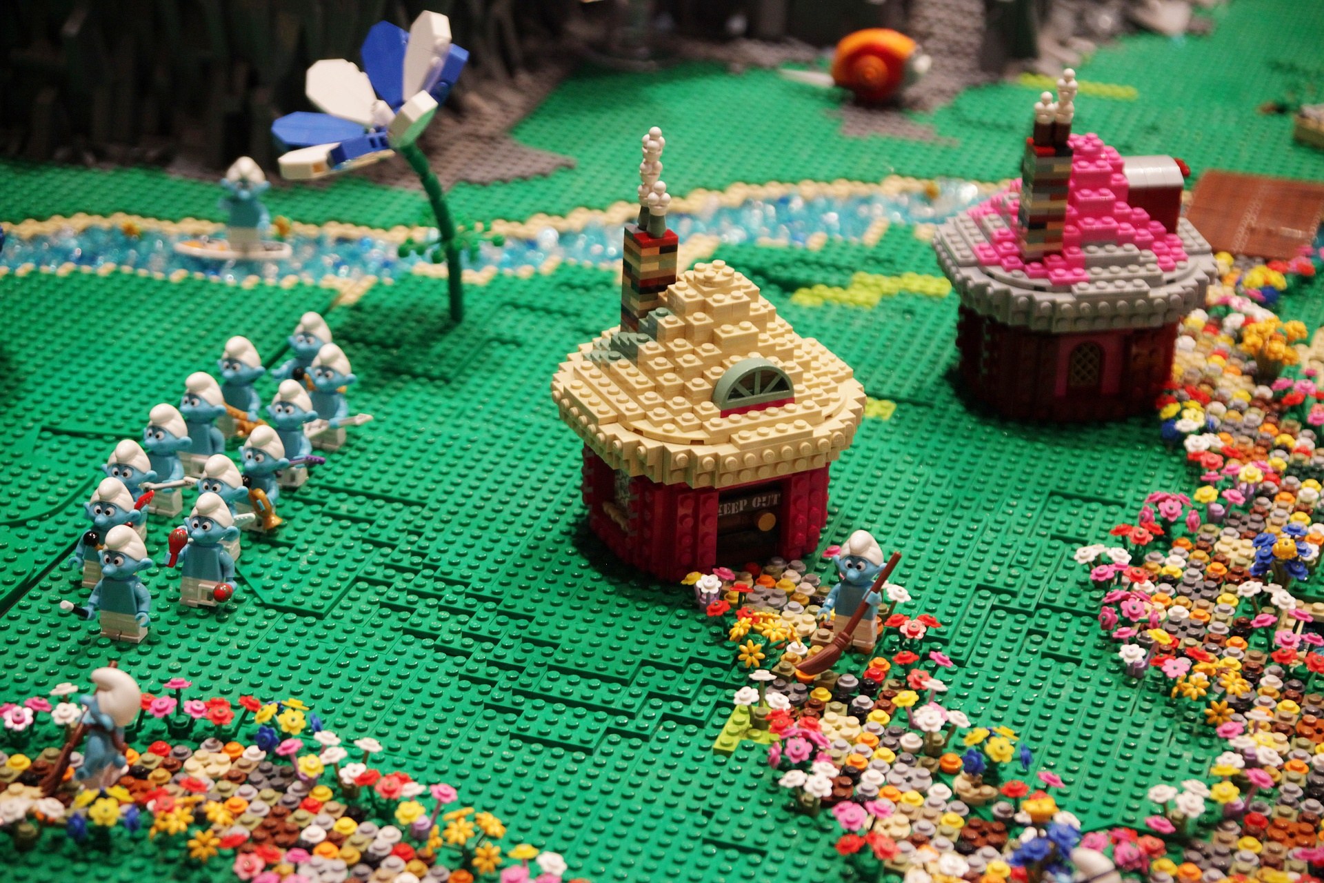 Ein Lego-Modell einer Kleinstadt mit bunten Blumen, Spielzeugen, Häusern, Pflanzen und anderen Gegenständen vor einem leicht unscharfen Hintergrund.