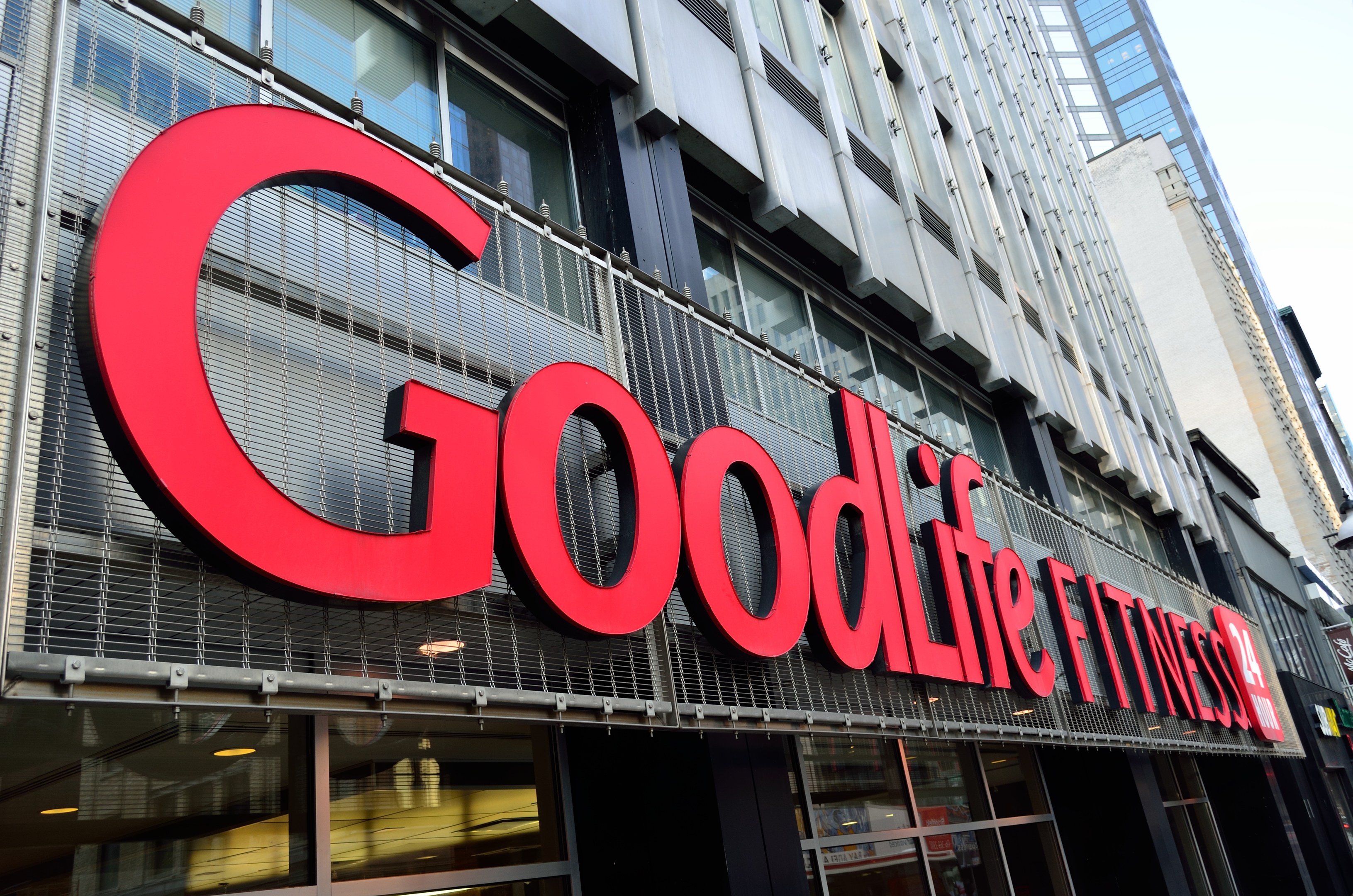 Außenansicht eines Goodlife Fitness Studios in New York City mit Glaswänden, einem Namensschild, benachbarten Gebäuden und Himmel im Hintergrund.