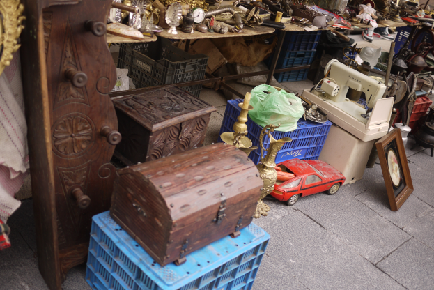 Ein Flohmarkt mit verschiedenen Artikeln, darunter Holzkisten, ein Spielzeugauto, eine Nähmaschine, ein Foto Rahmen, eine Uhr und andere Gegenstände auf Tischen.
