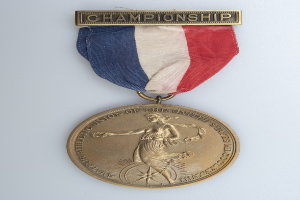 Goldmedaille mit rot-weiß-blauem Band, beschriftet mit 'Championship' und einem Personenbild.