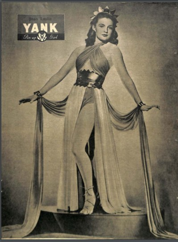 Ein Schwarz-Weiß-Foto der Schauspielerin Joan Leslie in einem langen, hochgeschlossenen Kleid mit langen Ärmeln, die selbstbewusst auf einer Bühne steht, mit geschlossenen Augen, eingerahmt von einem Photo-Rahmen und mit der Aufschrift 'Joan Leslie' oben.
