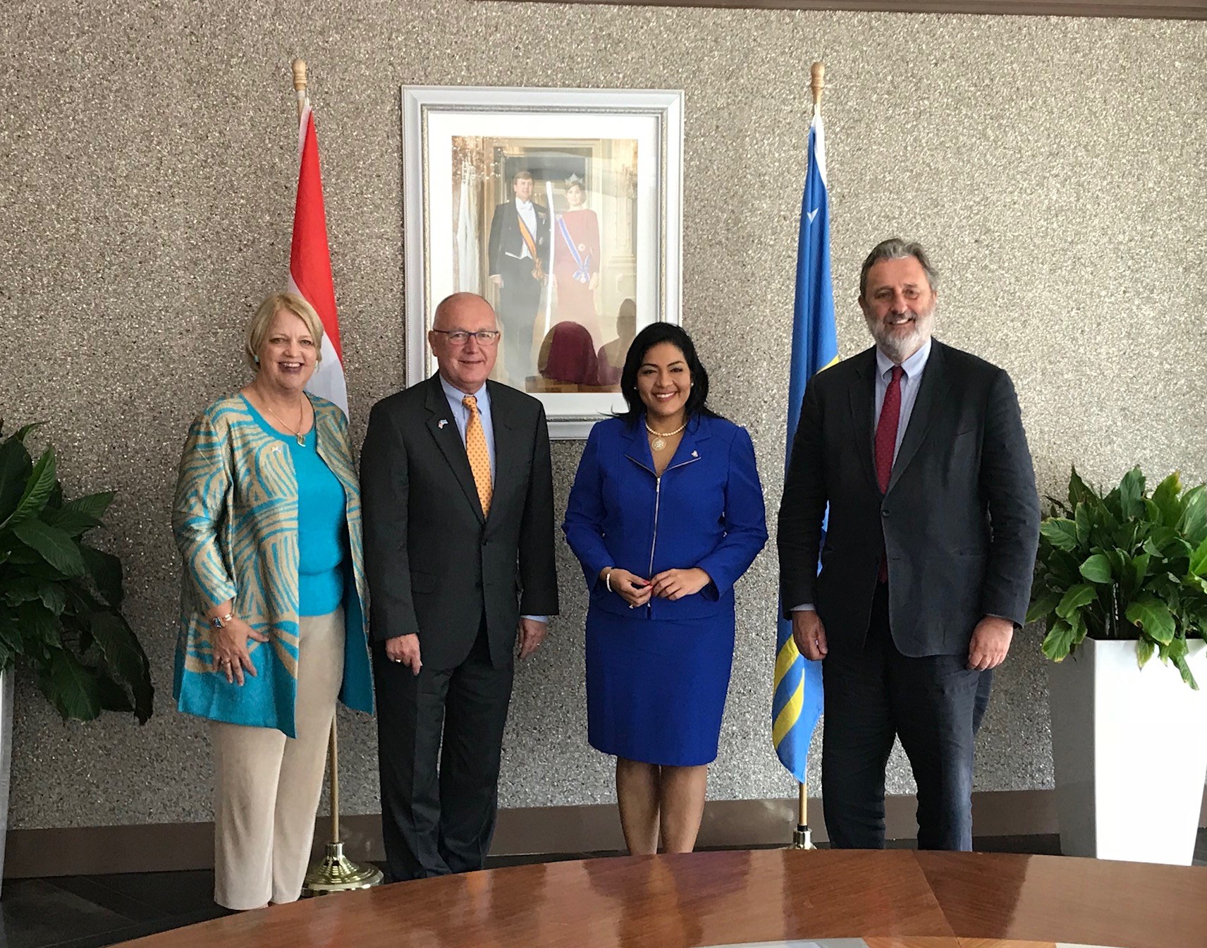 Eine Gruppe von Menschen, die um einen Tisch mit Papieren stehen und lächeln, umgeben von Flaggen, Topfpflanzen und einem Rahmenfoto an der Wand, was die Unterzeichnung eines U.S.-Kanada-Memorandums angibt.