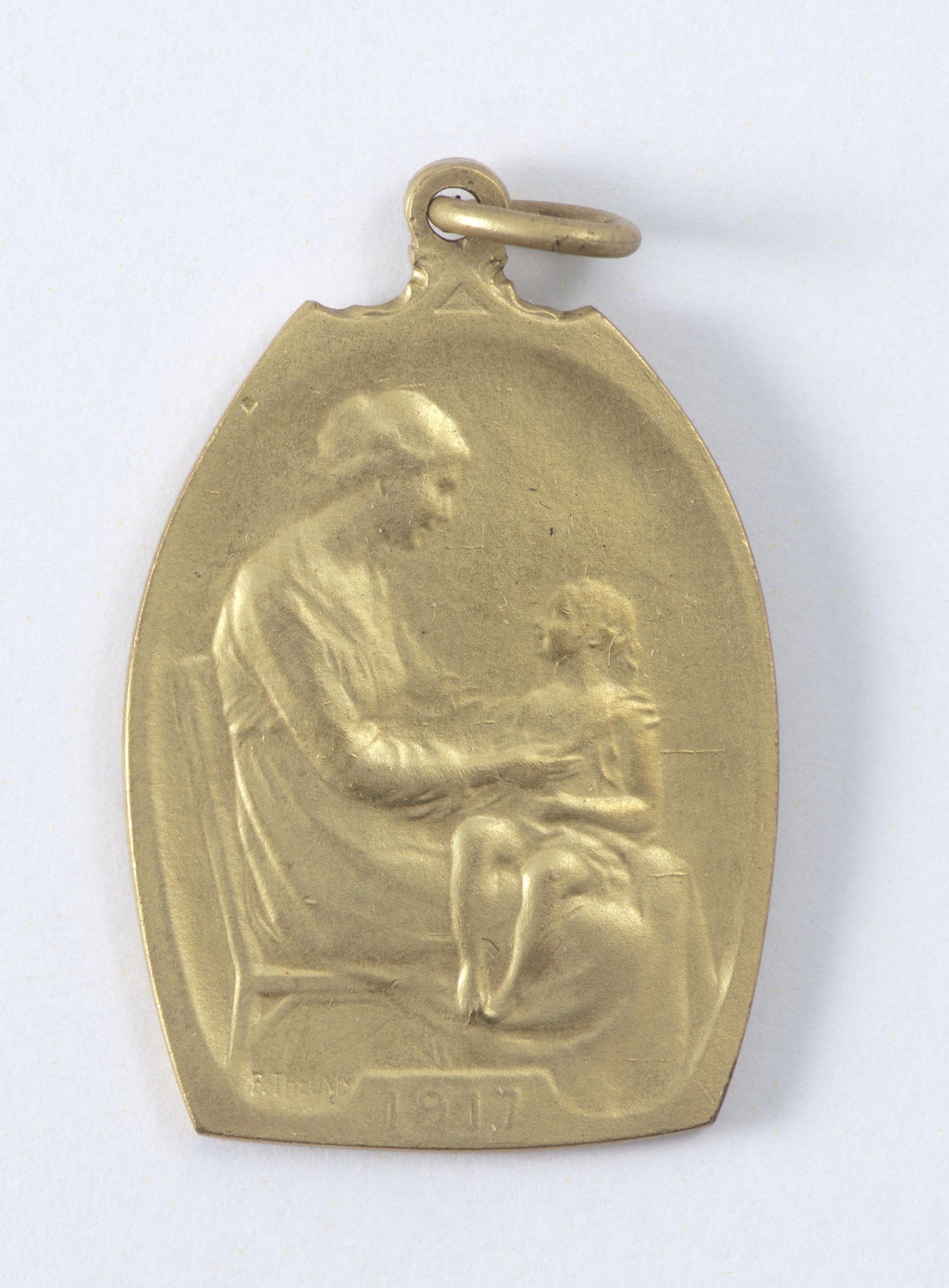 Goldmedaille mit einer Reliefdarstellung einer Frau in einem weißen Kleid mit einem Dutt, die ein Kind hält und beide sich gegenseitig sanft anschauen, beschriftet mit 'Mutter und Kind' in Schreibschrift.