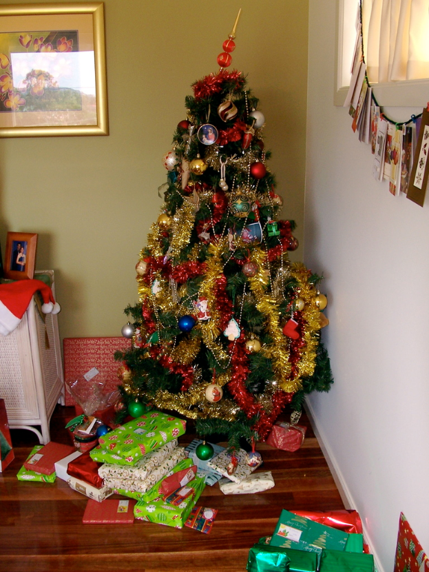 Ein geschmückter Weihnachtsbaum auf der rechten Seite mit Geschenken darunter, ein Foto Rahmen an der linken Wand und ein Vorhang am rechten Fenster.