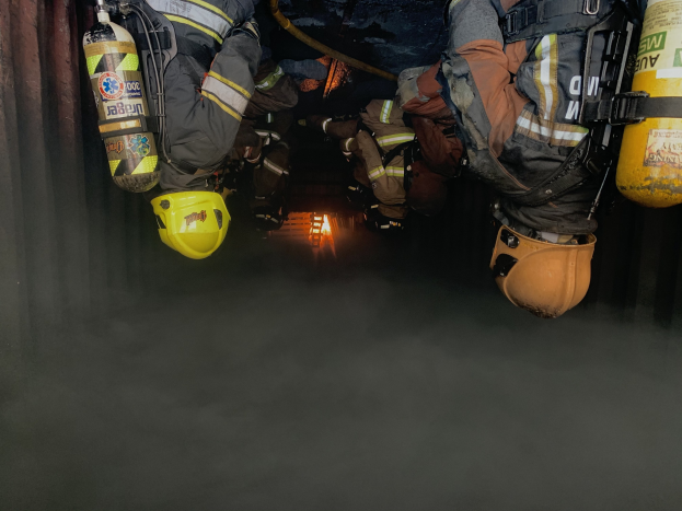 Feuerwehrleute in Schutzausrüstung und Atemschutz arbeiten in einem raucherfüllten Tunnel mit einer Lichtquelle im Hintergrund.