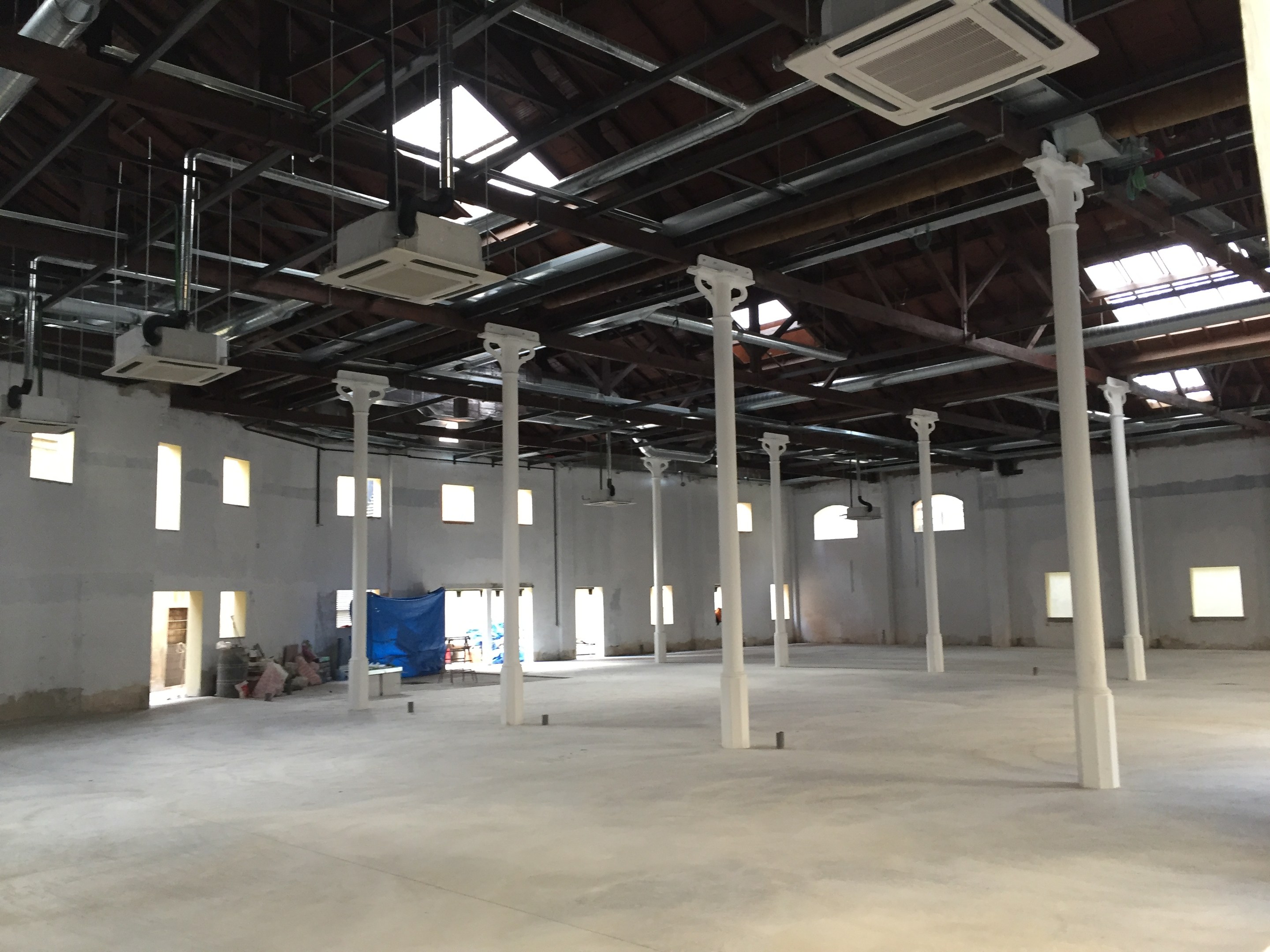 Industrielle Lagerhalle mit großen Fenstern, Säulen, Deckenleuchten und Klimaanlagen, verfügbar zur Miete.
