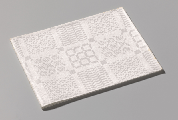 Ein weißes Buch mit einem sichtbaren QR-Code auf dem Cover liegt auf einer grauen Oberfläche.