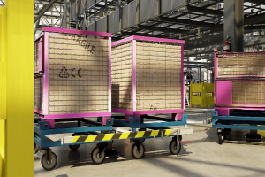 Großes Lager mit gestapelten Kisten auf Wagen, eine gelbe Säule links, ein Feuerlöscher rechts, Metallstangen im Hintergrund und sichtbarer Boden.