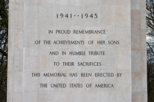 Ein Denkmal mit einer Tafel, auf der "In Stolzem Gedenken an die Taten ihrer Söhne und als Demutsvolles Gedenken an ihre Opfer" steht, vor einem Hintergrund aus Bäumen und einem klaren blauen Himmel.