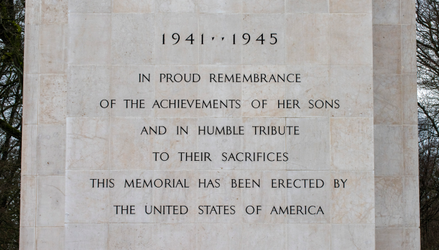 Ein Denkmal mit einer Tafel, auf der "In Stolzem Gedenken an die Taten ihrer Söhne und als Demutsvolles Gedenken an ihre Opfer" steht, vor einem Hintergrund aus Bäumen und einem klaren blauen Himmel.