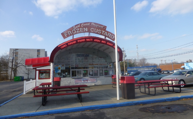 Ein Parkplatz mit Autos, Pfosten, Gebäuden, Bänken, einem Schuppen mit einer Tafel und Plakaten auf dem Schuppen.