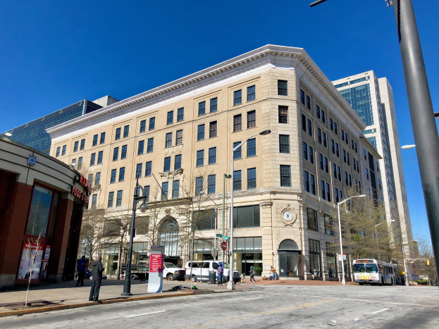 Großes Ziegelgebäude mit der Aufschrift "Washington Post Office" mit vielen Fenstern, umgeben von Straßenlaternen, Lampen, Fahrzeugen, Fußgängern, Schildern, Bäumen und einem bewölkten Himmel.
