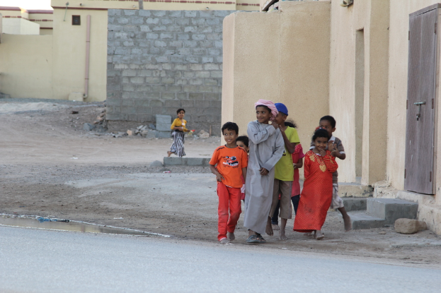 Eine Gruppe strahlender Kinder, die gemeinsam im Freien stehen, mit Gebäuden, Wasser, Felsen und einer Straße im Hintergrund.