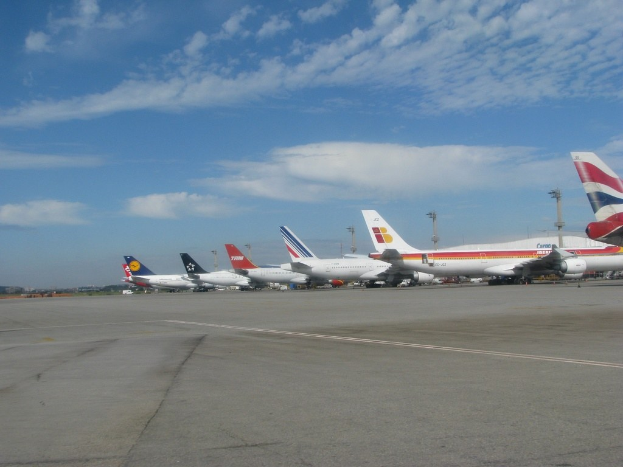Flugzeuge auf einer Start- und Landebahn mit Pfählen, Kabeln und Wolken am Himmel.