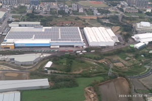 Luftaufnahme eines großen Industriegebiets mit Gebäuden, Bäumen, Gras, Straßen, Fahrzeugen, Polen und Türmen sowie einem Wasserzeichen in der rechten unteren Ecke, das darauf hinweist, dass es sich um die erste Solarstromanlage in Singapur handelt.