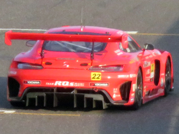 Ein leuchtend roter Porsche 911 GTS Rennauto mit einer großen Heckflosse und Spoiler, der auf einer Rennstrecke fährt.