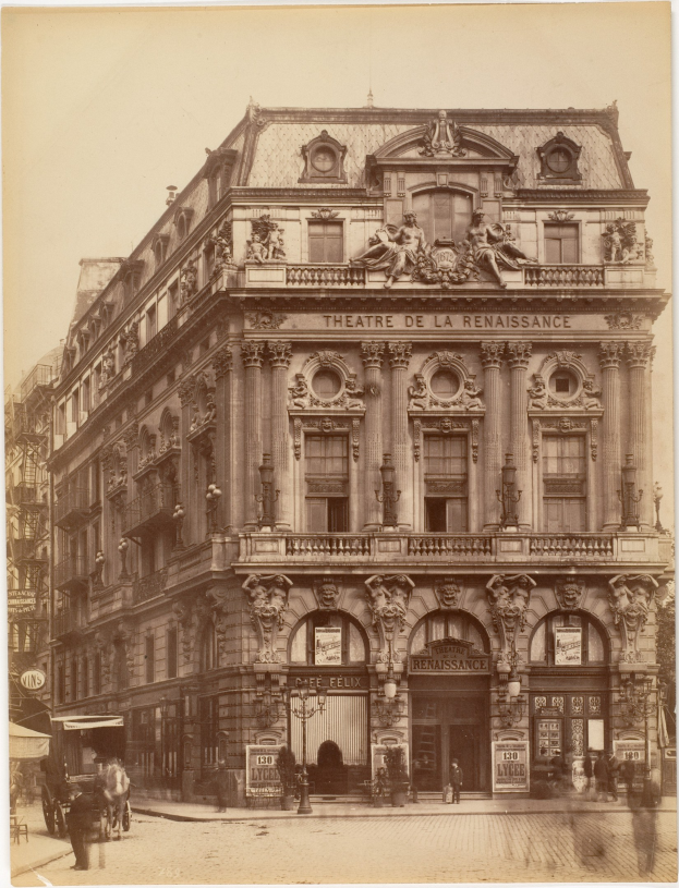 Schwarz-weiß-Fotografie des Théâtre de la Renaissance in Paris mit einer Fassade mit Fenstern, Säulen, Bögen und Skulpturen, mit einigen Menschen und Fahrzeugen auf der Straße davor und sichtbarem Himmel im Hintergrund.