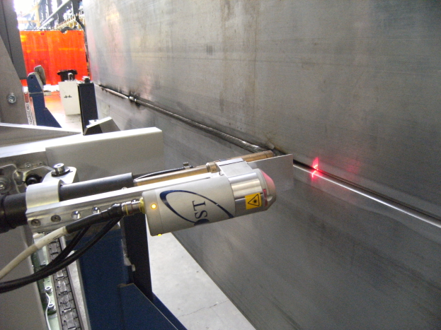 Eine Laserschneidemaschine in einer Fabrik strahlt helles Licht aus, mit einer Wand auf der rechten Seite und ein paar Gegenständen im Hintergrund.