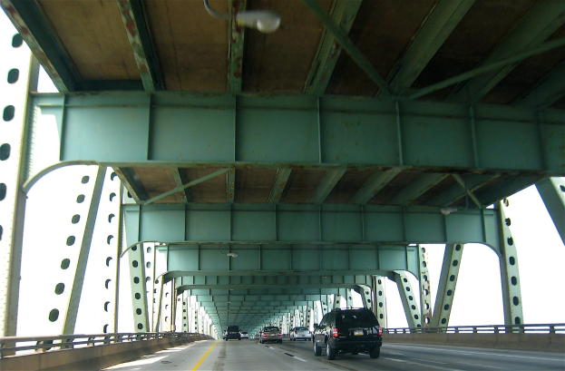 Ein Auto fährt über eine Hängebrücke mit Geländern auf beiden Seiten unter einem klaren blauen Himmel.