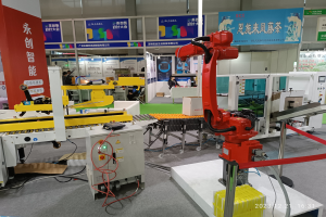 Eine Gruppe von Robotern auf einem Tisch in einer Fabrikumgebung umgeben von Maschinen, Kabeln, Leiterplatten und Beleuchtung, mit Menschen im Hintergrund.