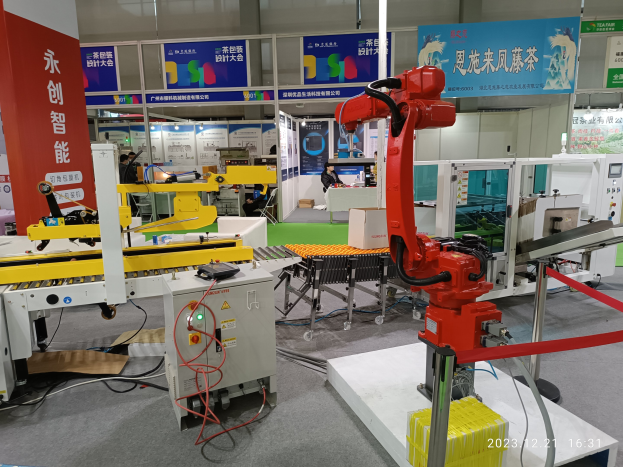 Eine Gruppe von Robotern auf einem Tisch in einer Fabrikumgebung umgeben von Maschinen, Kabeln, Leiterplatten und Beleuchtung, mit Menschen im Hintergrund.