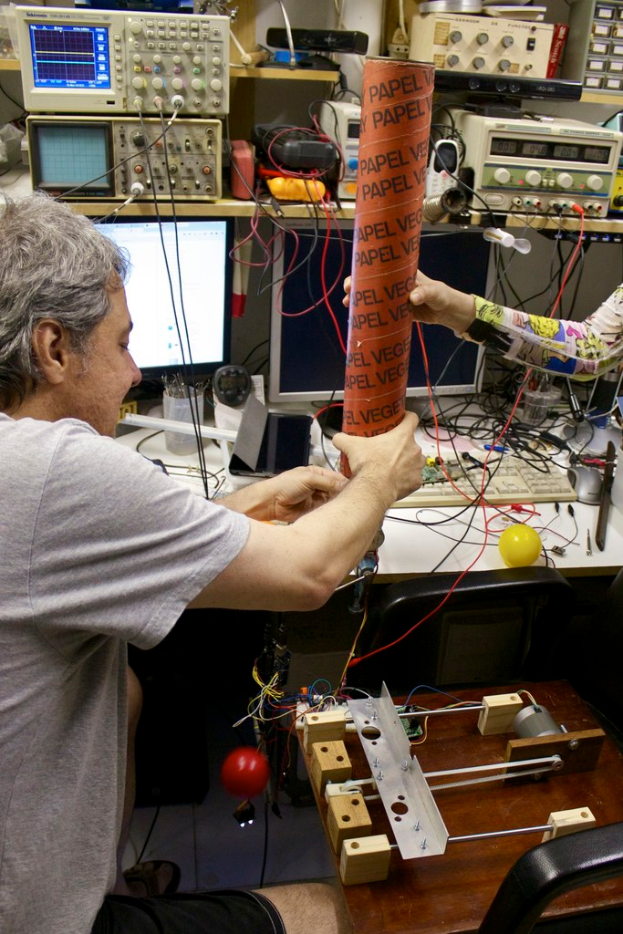 Ein Arbeitsplatz mit Maschinen, Kabeln, einem Computerbildschirm, einem Stifthalter, Menschen und einem Stressball.