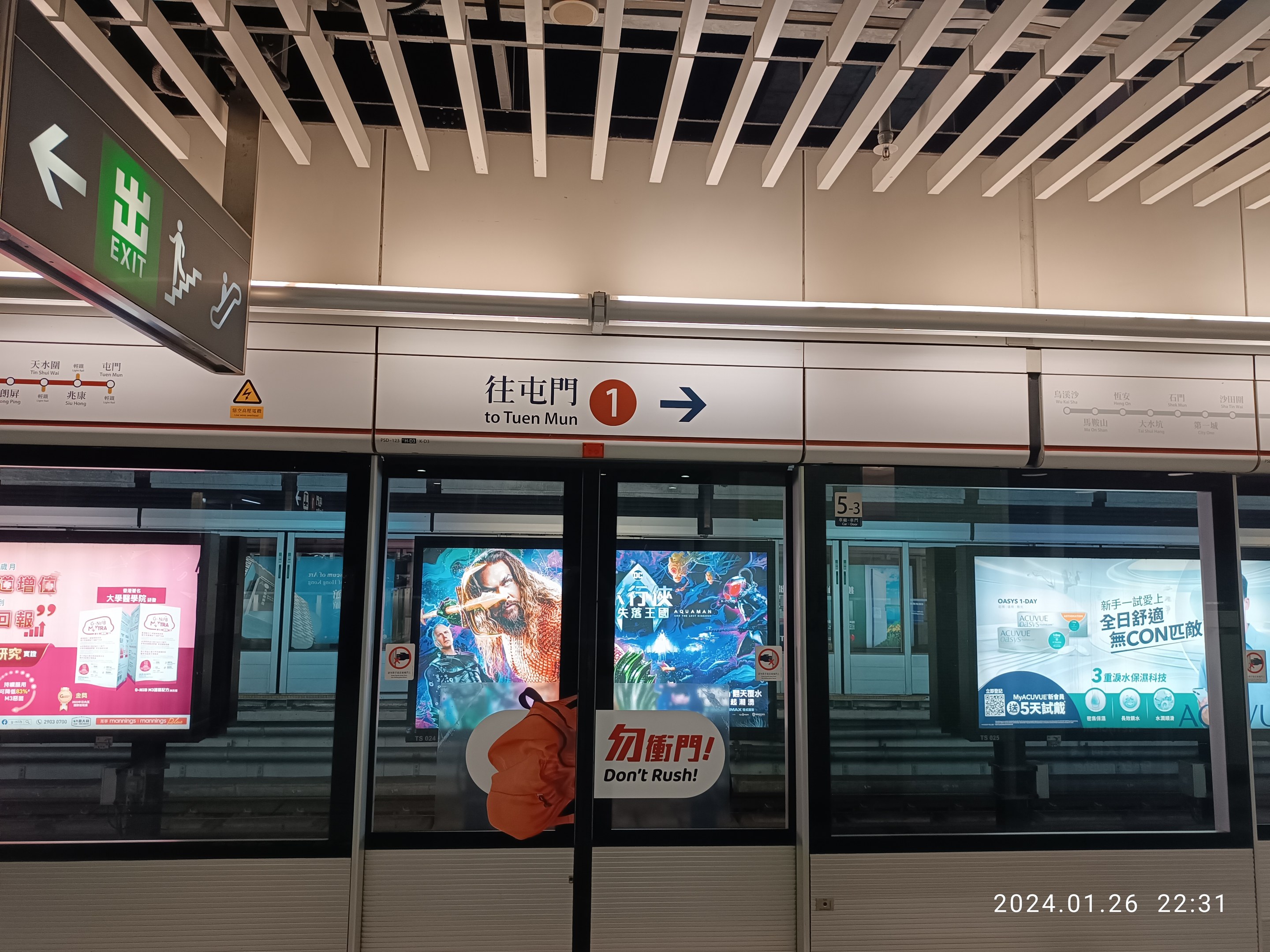Eine U-Bahn mit Glastüren und digitalen Bildschirmen an einem Bahnhof, mit Text- und Nummernschildern an der Wand und Deckenleuchten darüber.