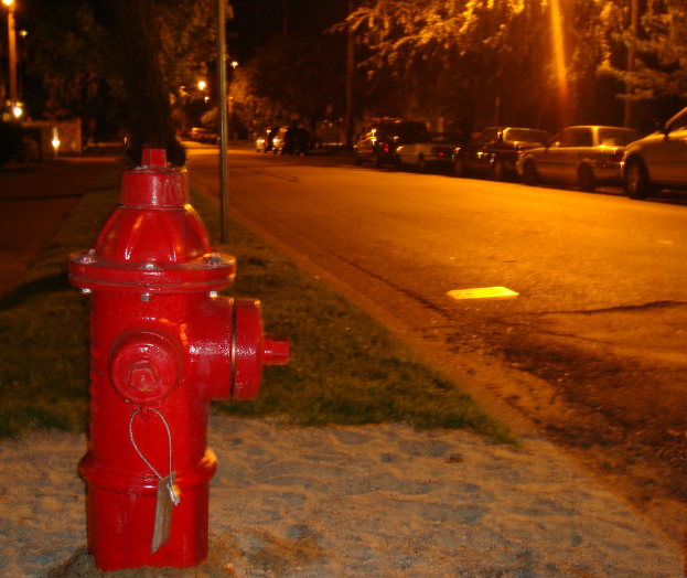 Ein Feuerhydrant an der Seite einer Straße, mit Autos und Bäumen im Hintergrund.