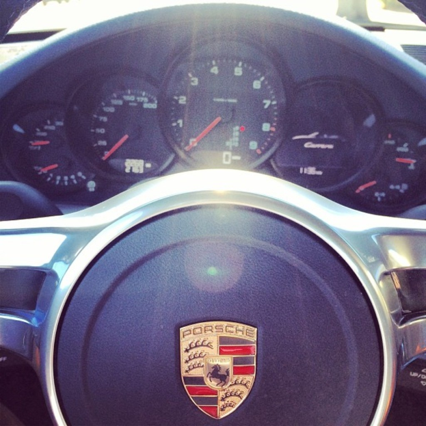 Ein Nahaufnahme-Bild des Armaturenbretts eines Porsche-Fahrzeugs, das den Tacho und das Lenkrad zeigt.