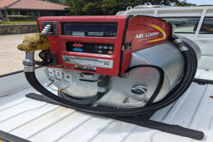 Ein Lastwagen mit einer Gasstation an der Rückseite parkt neben einem Haus, umgeben von Bäumen unter einem klaren blauen Himmel.