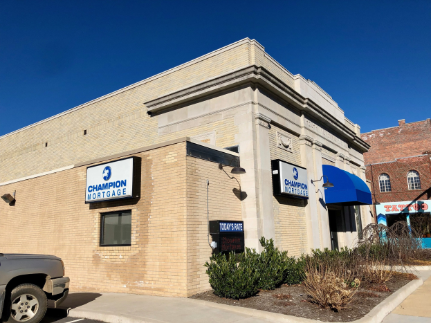 Ein zweistöckiges Gebäude mit vernagelten Fenstern, einem geparkten Auto, Topfpflanzen und Bäumen unter einem bewölkten Himmel, mit "Champion Mortgage, Inc."-Schildern an den Brettern.