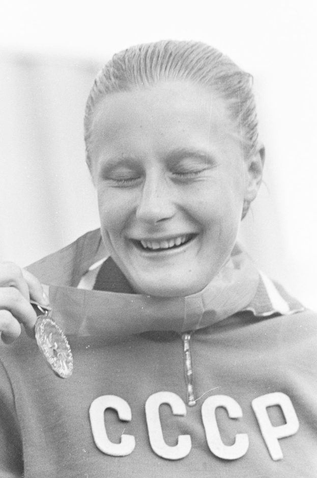 Eine Frau mit strahlendem Lächeln hält stolz eine Silbermedaille hoch, mit einem unscharfen Hintergrund, der auf sie und ihre Leistung hinweist.