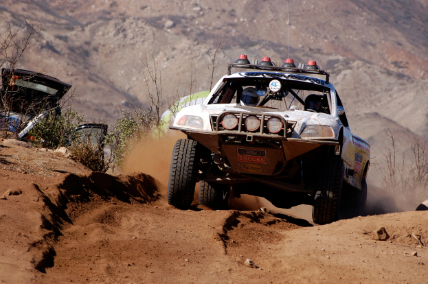 Ein weißes Auto fährt auf einer Straße mit grünen Pflanzen auf der linken Seite.