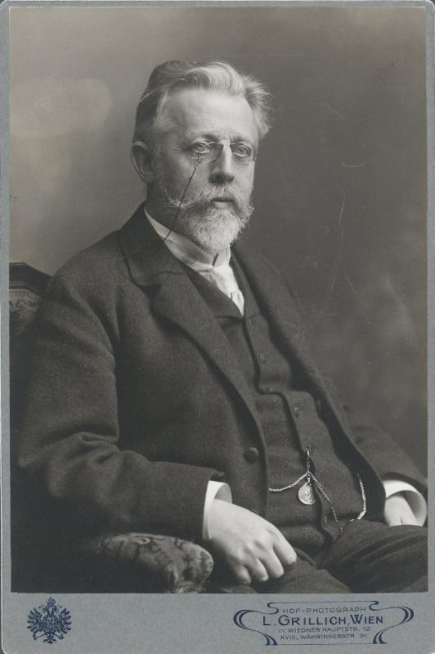 Schwarz-weiß-Fotografie eines bärtigen Mannes mit Brille, der auf einem Stuhl sitzt, mit Text unten, der ihn als "L. Grillich Wien, den Gründer der deutschen Revolution" identifiziert.