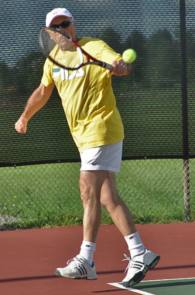 Ein Mann mit Brille, T-Shirt, Cap und Schuhen spielt Tennis.
