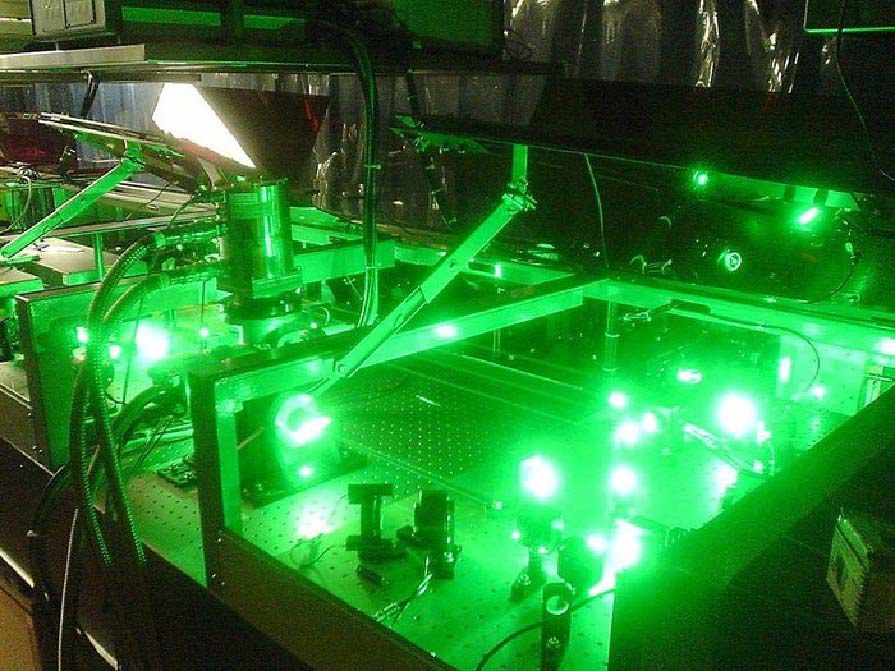 Eine Laser-Maschine auf einem Tisch, die grünes Licht abstrahlt, mit sichtbaren Komponenten und angeschlossenen Kabeln.