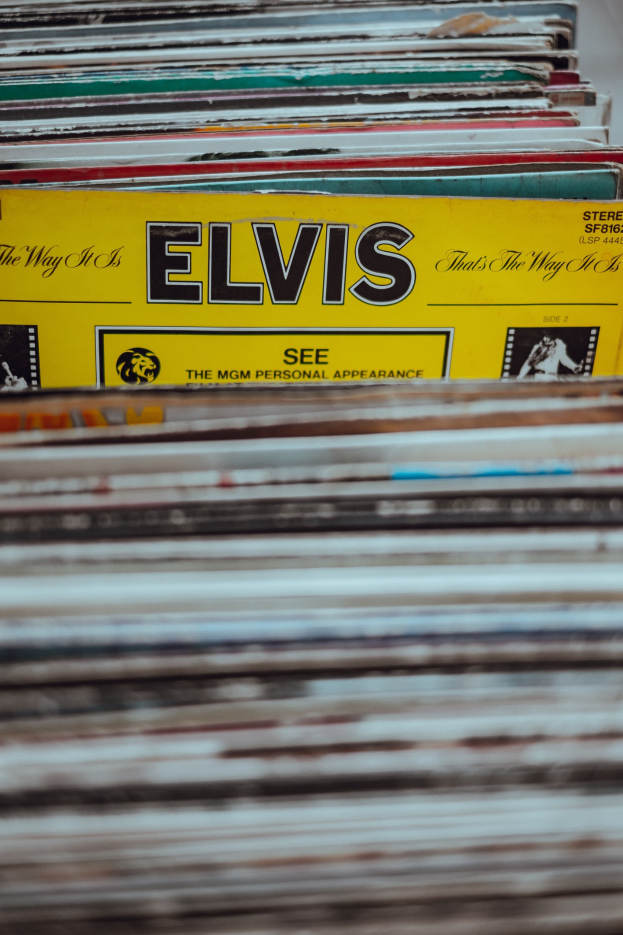 Ein ordentlicher Stapel Elvis-Presley-Platten mit sichtbaren Titeln steht auf einem Tisch, der Hintergrund ist leicht unscharf.