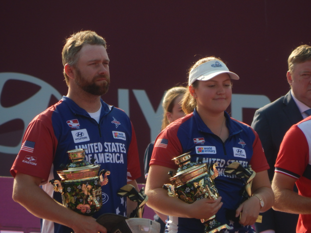 Eine Gruppe von Menschen, die Trophäen halten, mit einem "Weltarcherie-Meisterschaften"-Schild im Hintergrund.