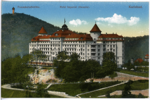Eine alte Postkarte, die das Hotel Imperial in Karlsbad, Deutschland zeigt, ein großes Gebäude mit zahlreichen Fenstern, umgeben von Bäumen, Pflanzen und Gras, mit einem Weg im Vordergrund, Hügel im Hintergrund und einem bewölkten Himmel, mit Text oben auf dem Bild.