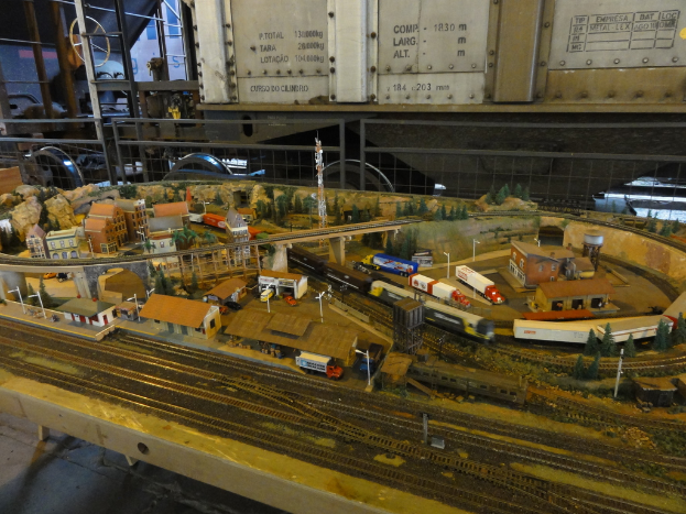 Eine Miniaturszene auf einem Tisch mit einer Eisenbahnschiene, einem Zug, Gebäuden, Fahrzeugen, einer Brücke, einem Turm und Bäumen.