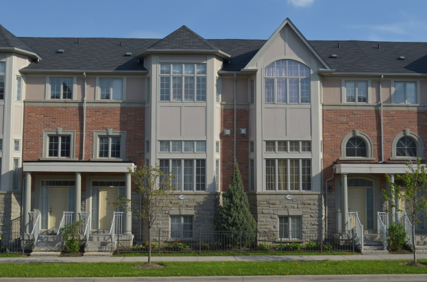 Eine Reihe von Stadthäusern in einer Wohngegend mit Fenstern, Türen, Säulen, Geländern, Treppen, Pflanzen, Bäumen, Gras, einer Straße im Vordergrund und dem Himmel im Hintergrund.