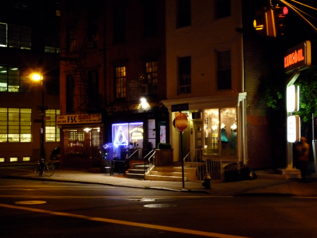 Eine Stadtansicht mit Gebäuden, beleuchteten Geschäften, einer Treppe, Bäumen entlang der Straße, einer Straße mit einem Fahrrad und einer Ampel.