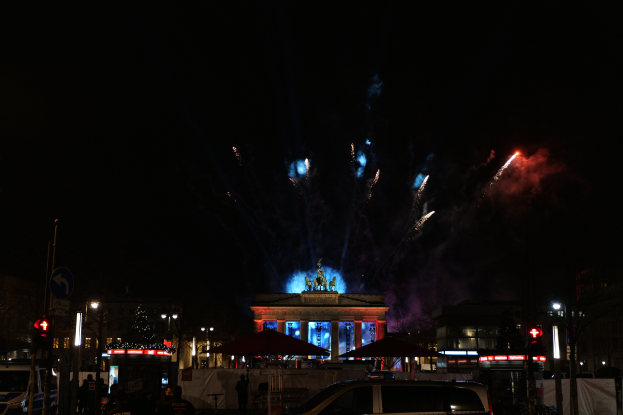 Ein vor dem Reichstagsgebäude in Berlin geparktes Auto mit Menschen drumherum und Feuerwerk am Nachthimmel.