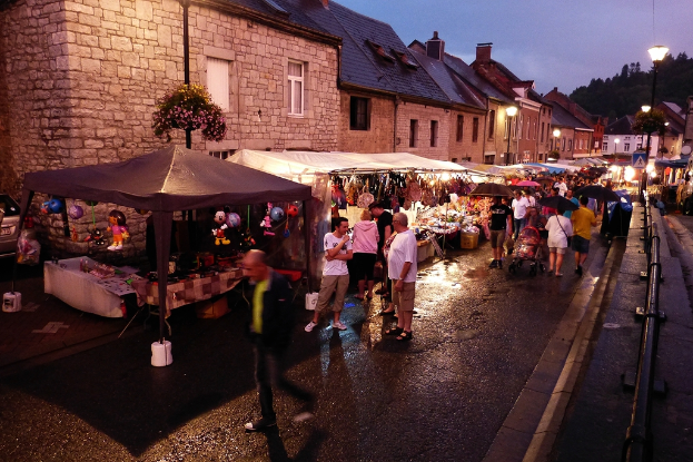 Eine Gruppe von Menschen auf der Straße mit Geschäften, Schirmen, hängenden Spielzeugen, Taschen, Gebäuden mit Fenstern, Bäumen, Straßenlaternen und Barrieren.