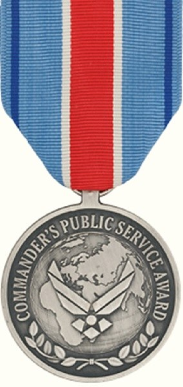 Eine silberne Medaille mit rot-weiß-blauem Band, beschriftet mit 'Commander's Public Service Award', vor weißem Hintergrund.