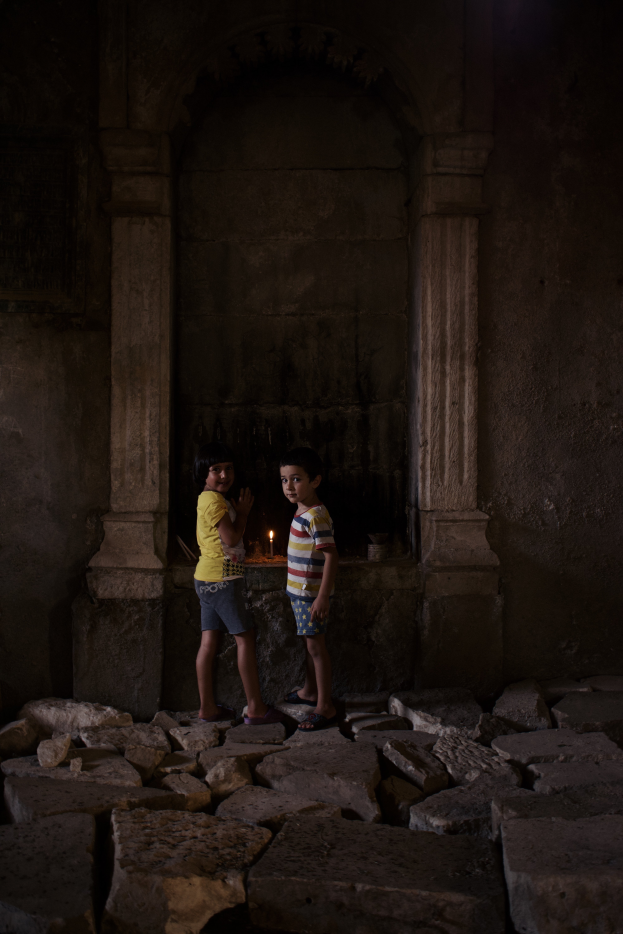 Zwei junge Jungs stehen vor einer Steinwand, beleuchtet von einer einzelnen Lichtquelle, beide tragen Schuhe.