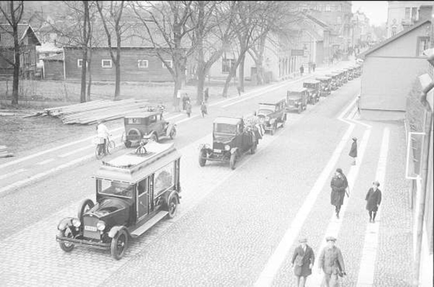 Schwarze und weiße Straßenszene in Berlin aus den 1930er-1940er Jahren, die vintage-Autos, Fußgänger, Gebäude mit Fenstern, Bäume und einen klaren Himmel zeigt.