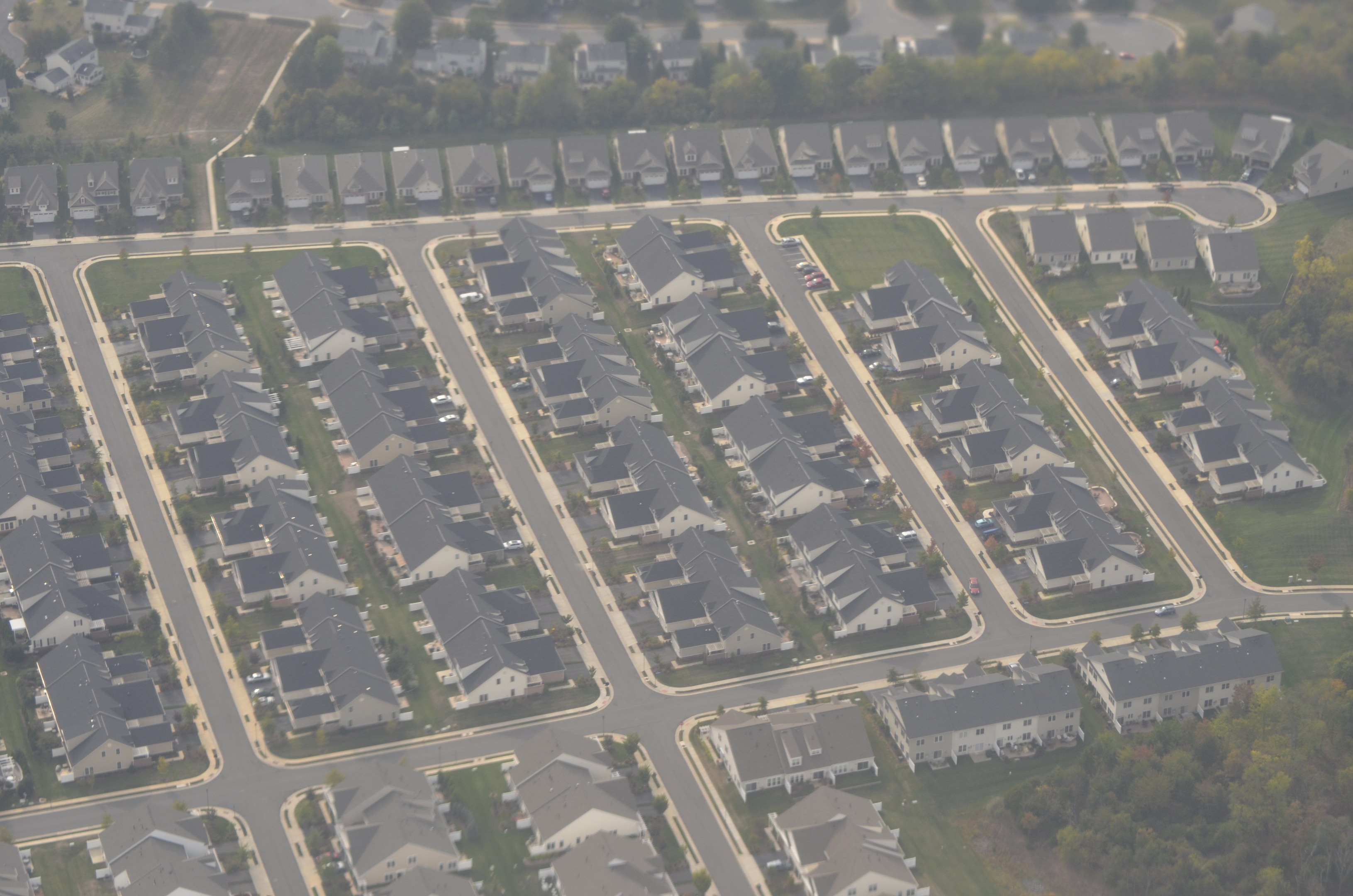 Luftaufnahme eines Wohnviertels mit Häusern, Bäumen, Gras, Straßen und Fahrzeugen.