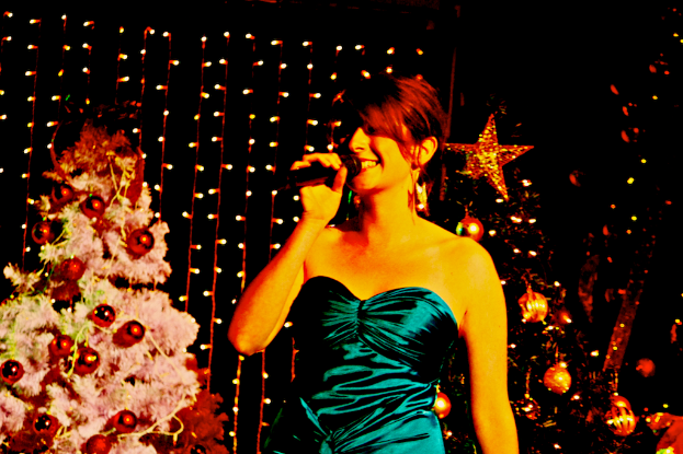 Eine Frau steht mit einem Mikrofon in der Hand vor Weihnachtsb├╝umen und Lichtern